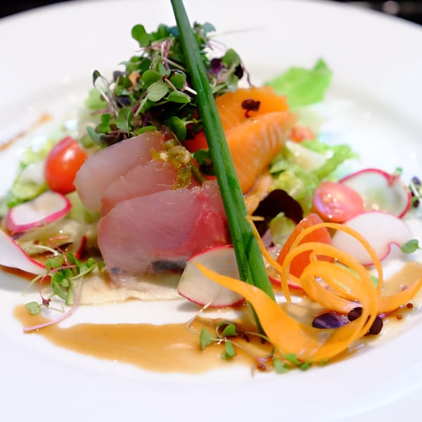 A vibrant Tsuru Sushi salad with sliced fish, cherry tomatoes, radishes, and carrot ribbons.