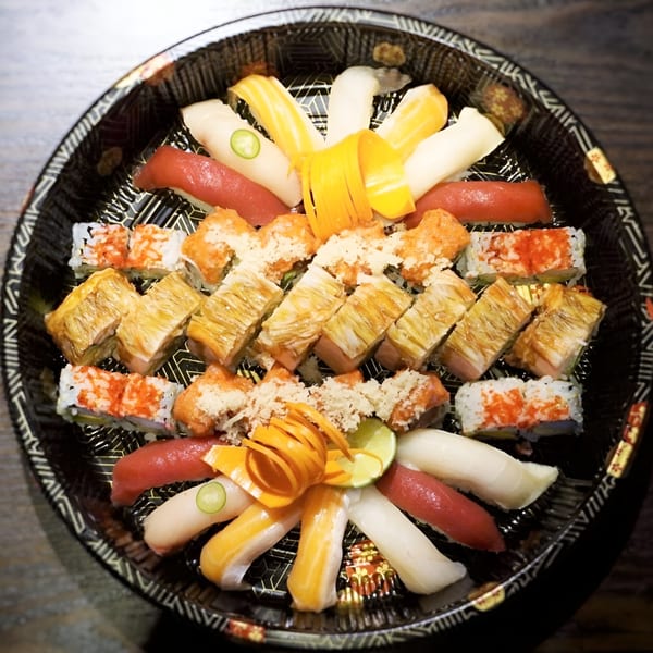 A large platter of assorted Tsuru Sushi rolls and nigiri, garnished with lime and carrot curls.