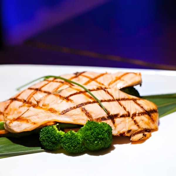 Grilled salmon fillets with char marks, broccoli florets, and green garnish on a white plate.